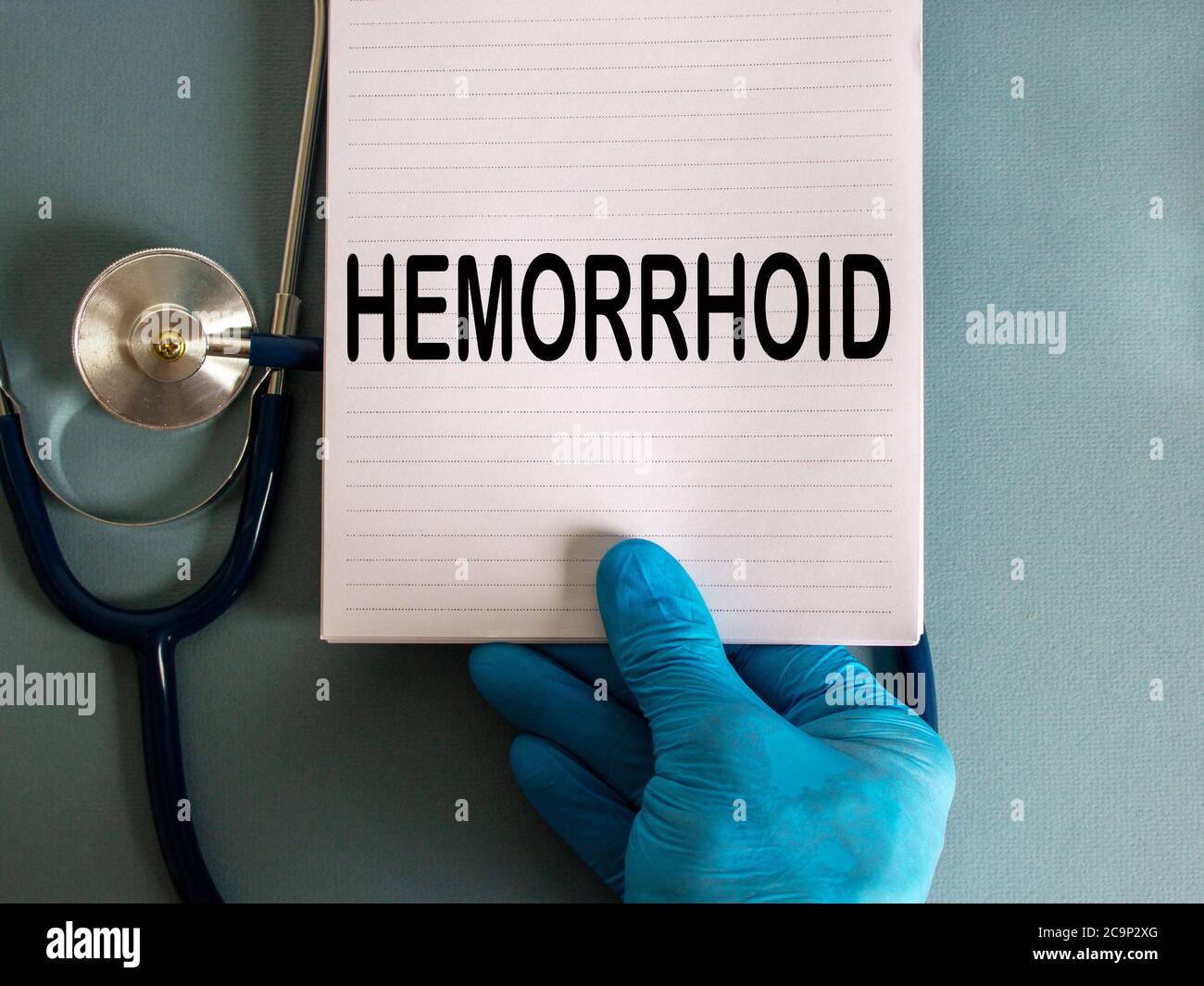 Main dans un gant bleu, carte blanche avec le mot « hémorroïde » et stéthoscope. Banque D'Images