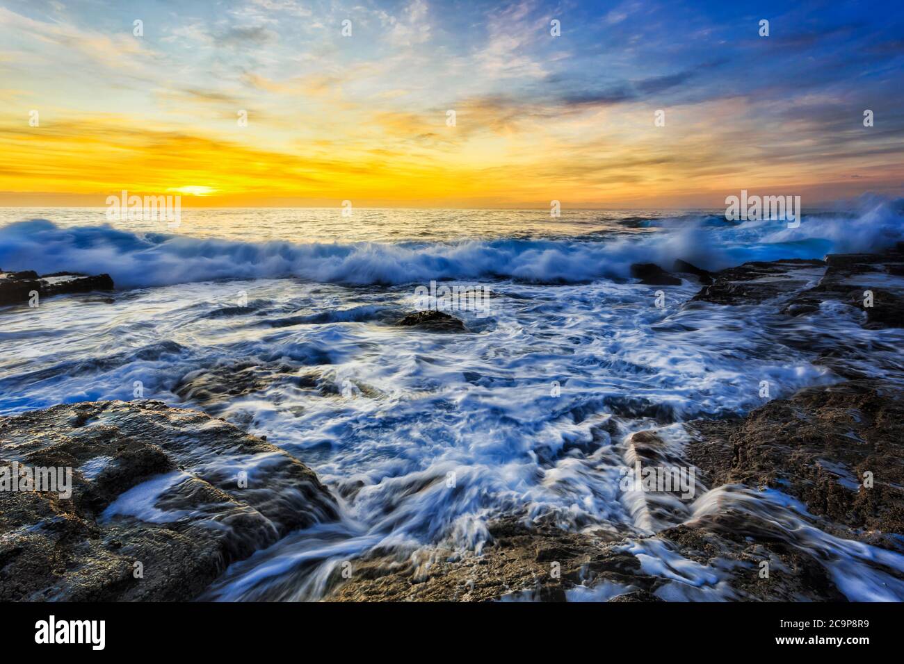 Petite vague se déroulant sur les rochers de grès des plages du nord de Sydney au lever du soleil - Pacific Ocean Shore, Australie. Banque D'Images