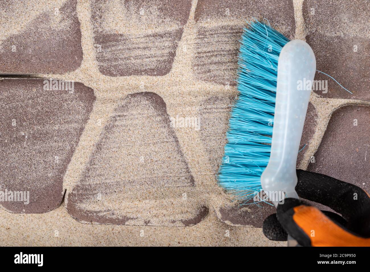Pose de pavés sur du sable. Balai et sable pour lisser les joints dans la chaussée. Arrière-plan clair. Banque D'Images