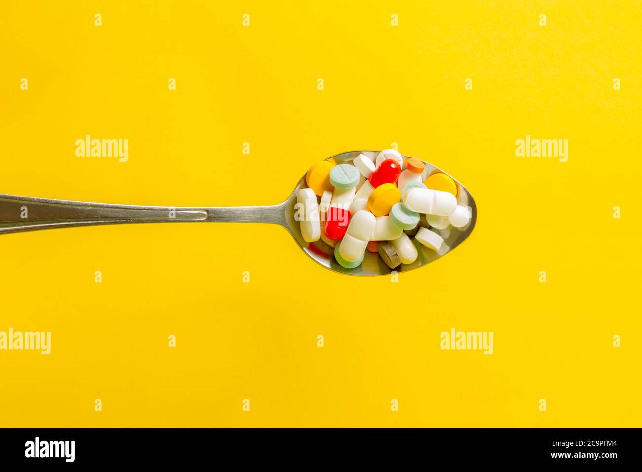Cuillère pleine de pilules sur fond jaune. Concept d'automédication et d'abus de drogues. Banque D'Images
