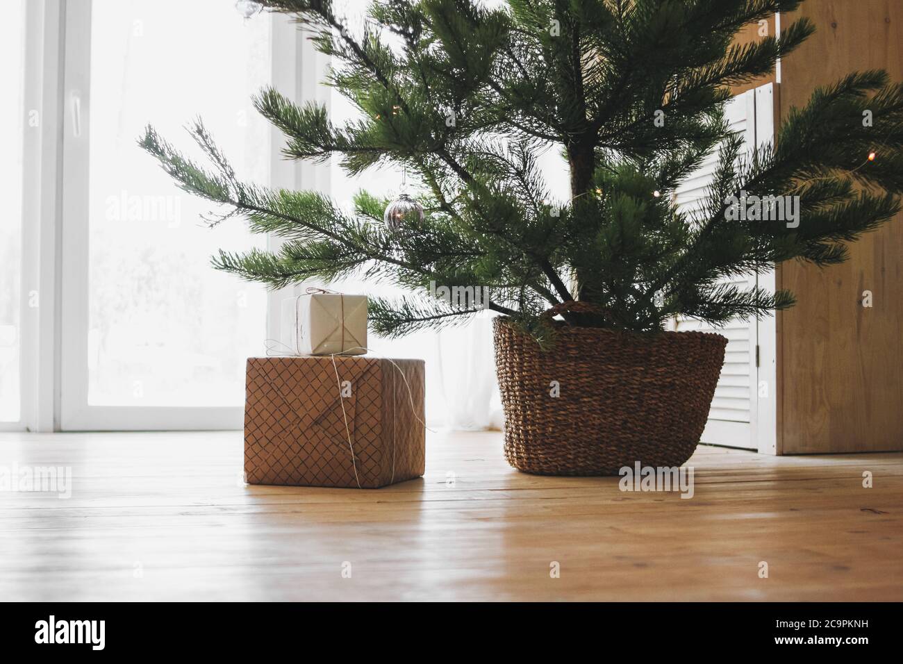 PIN de noël naturel dans un bascette en osier avec boîtes-cadeaux en papier artisanal sur parquet Banque D'Images