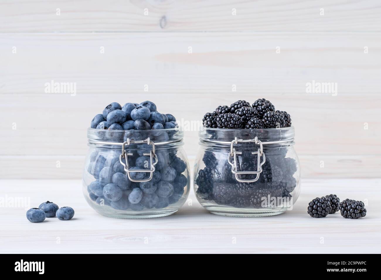 Bleuets et mûres dans un bol en verre sur une table en bois, fond de tableau blanc. Une baie dans une verseuse en verre. Concept de cuisine végétarienne Banque D'Images