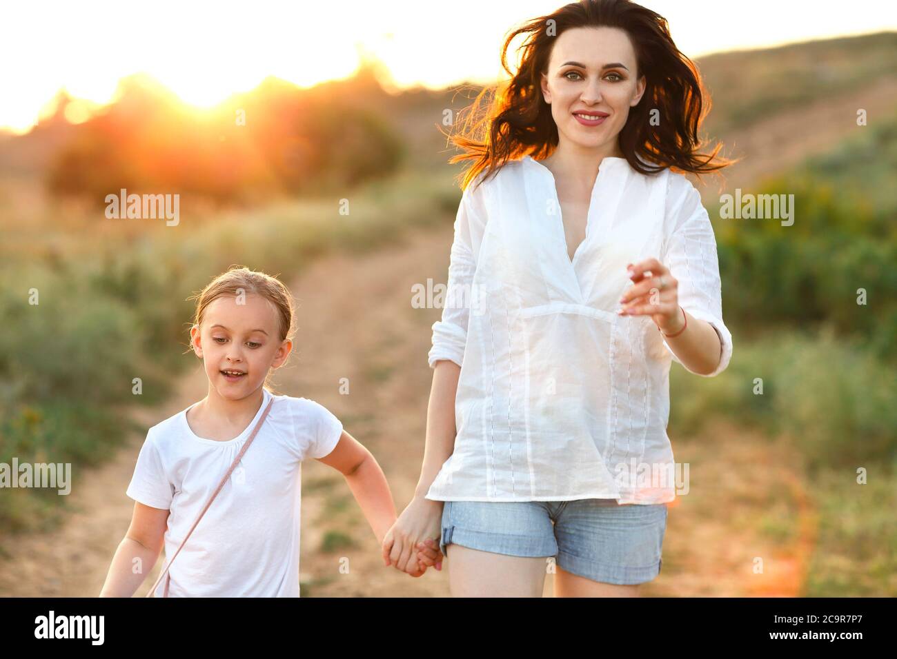 Jeune femme et petite fille tenant les mains et marchant le long de la route de sable au coucher du soleil pendant le week-end Banque D'Images