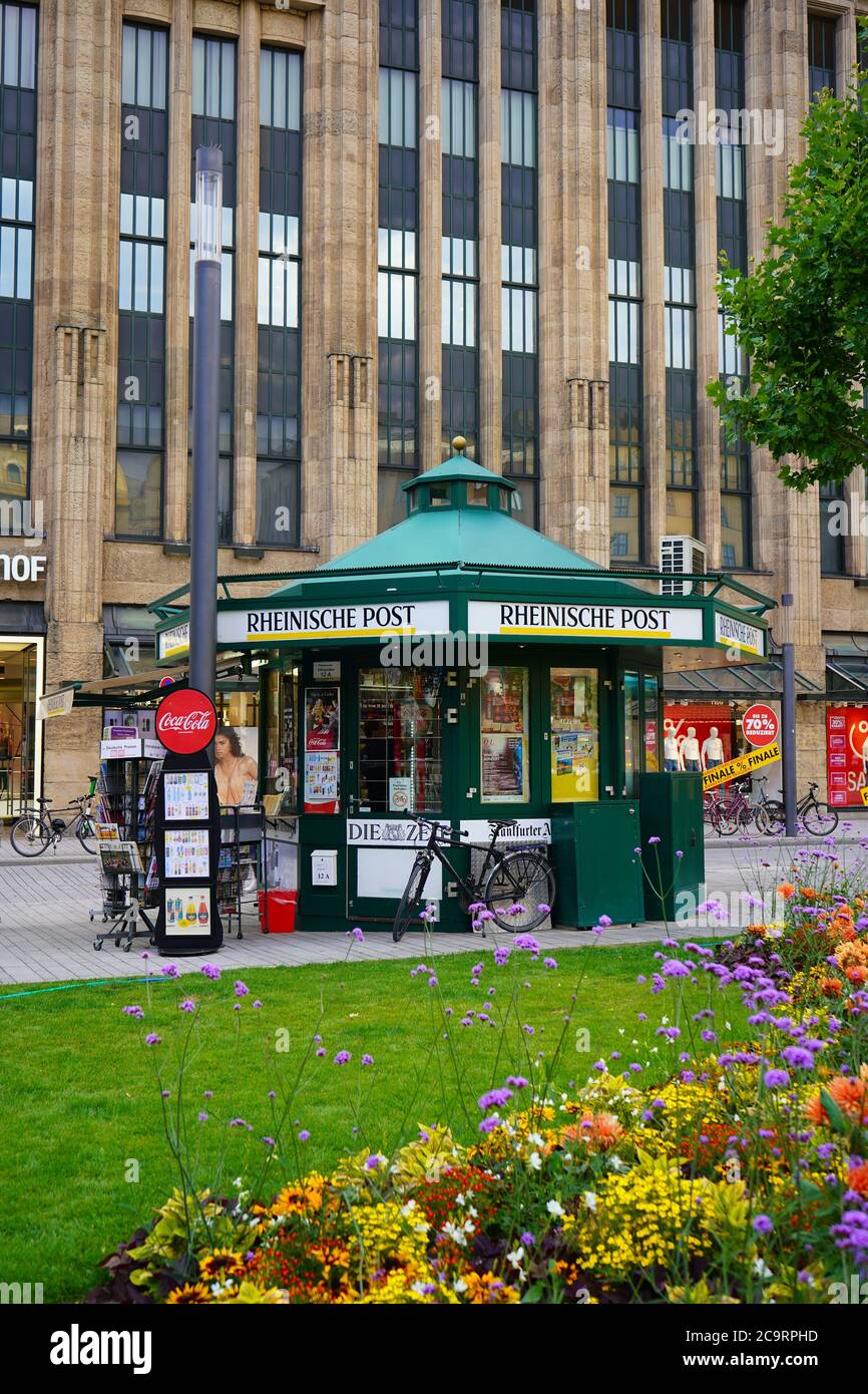 Kiosque à journaux en face du grand magasin Kaufhof à Königsallee à Düsseldorf lors d'une belle journée d'été avec fleurs d'été et prairie verte. Banque D'Images