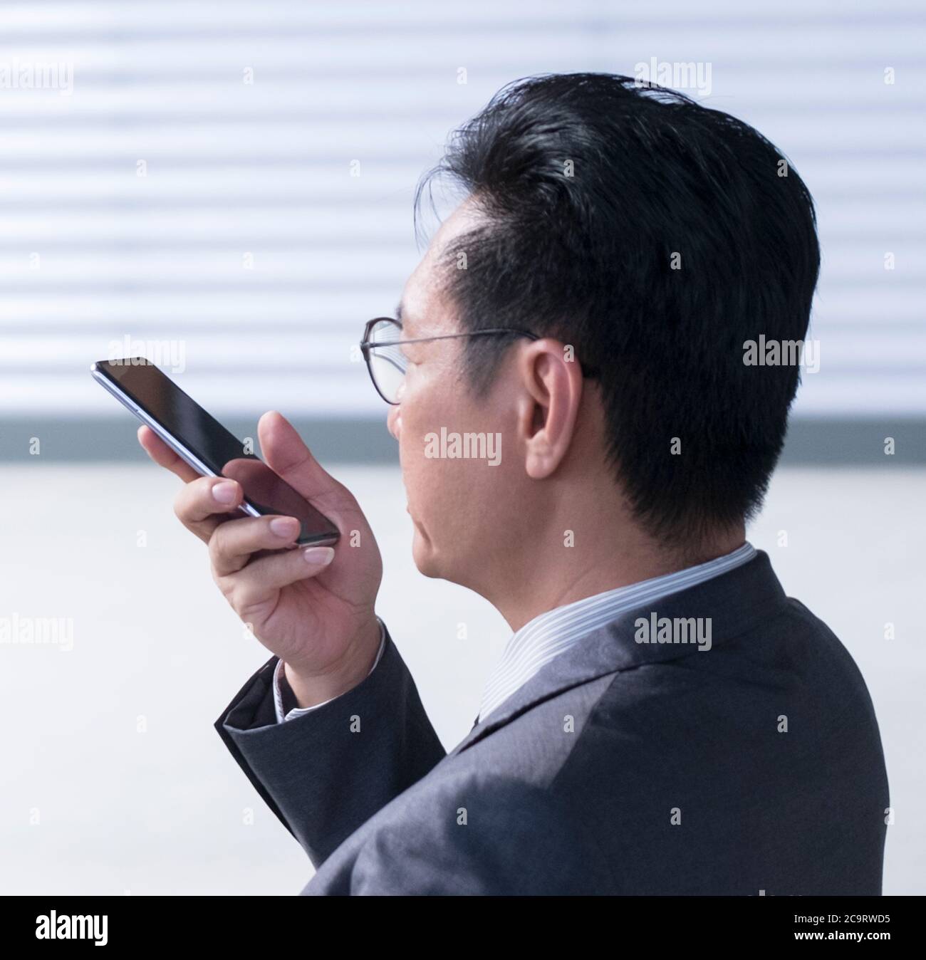 Homme d'affaires chinois utilisant un téléphone portable pour laisser un message vocal. Gros plan, vue de la tête. Banque D'Images