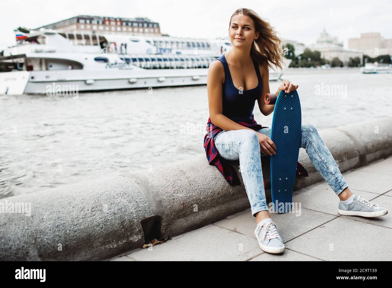 belle femme blonde posant avec un skateboard dans un parc de la ville Banque D'Images