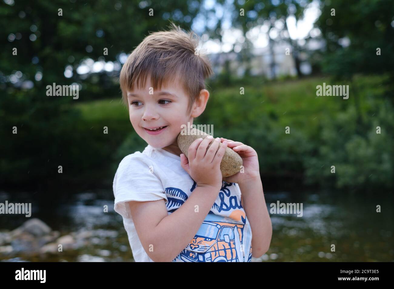 Garçon jouant avec des pierres à côté de ruisseau Banque D'Images