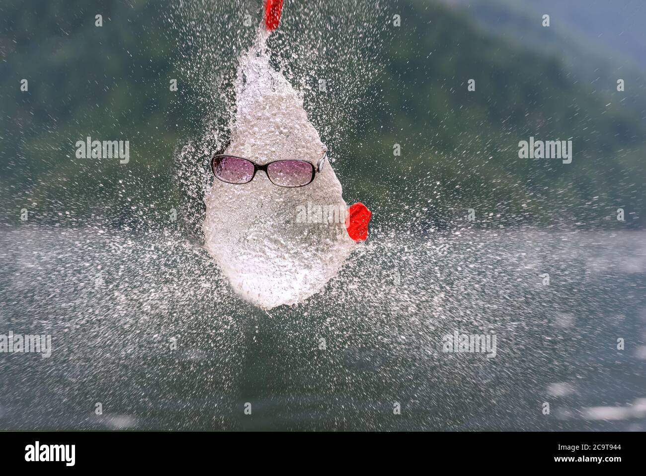 Résumé drôle figure humoristique avec un visage dans des lunettes de soleil fait d'eau et de spray, résultant d'un ballon d'éclatement rempli d'eau contre Banque D'Images
