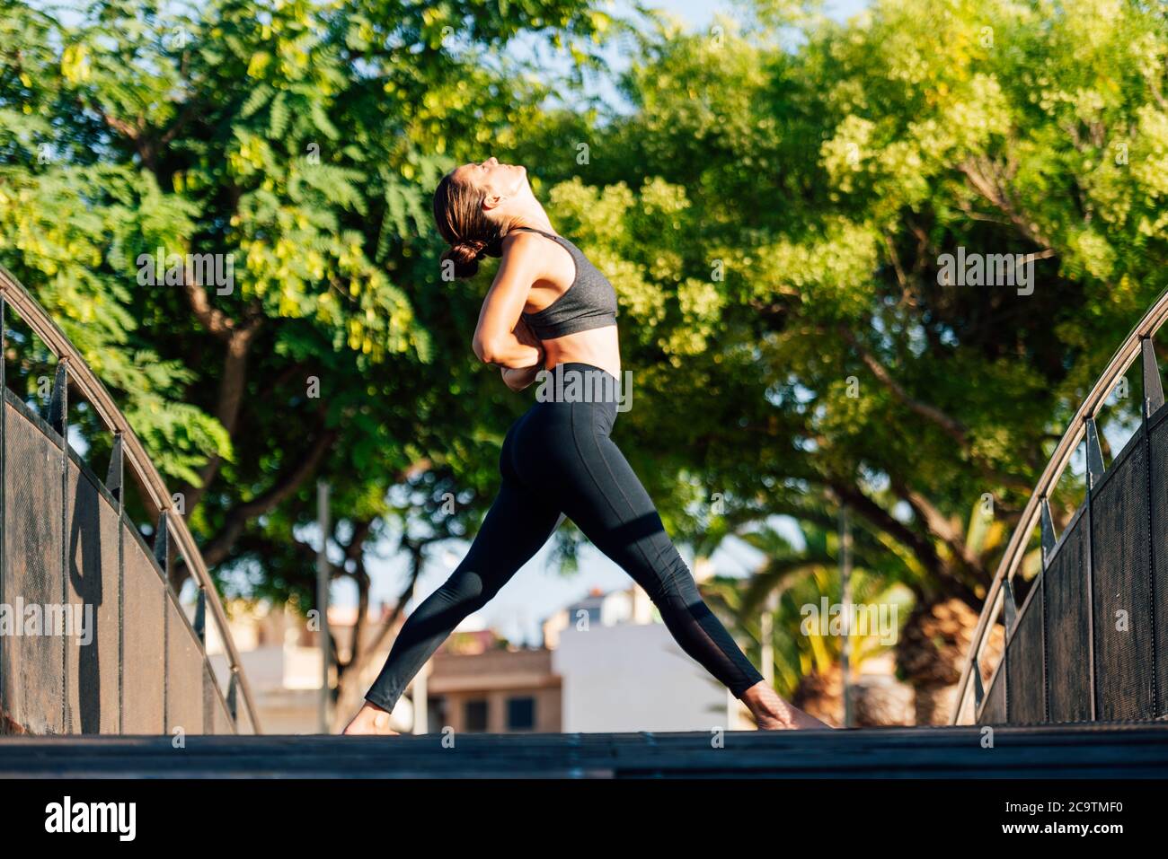 jeune femme faisant des exercices sur un pont en cuivre extérieur entouré de jardins Banque D'Images
