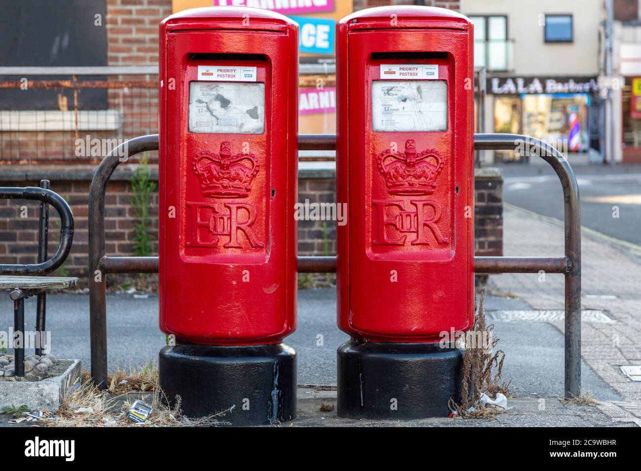 Deux boîtes postales Royal rouges côte à côte sur une rue avec un autocollant indiquant la boîte postale prioritaire Banque D'Images