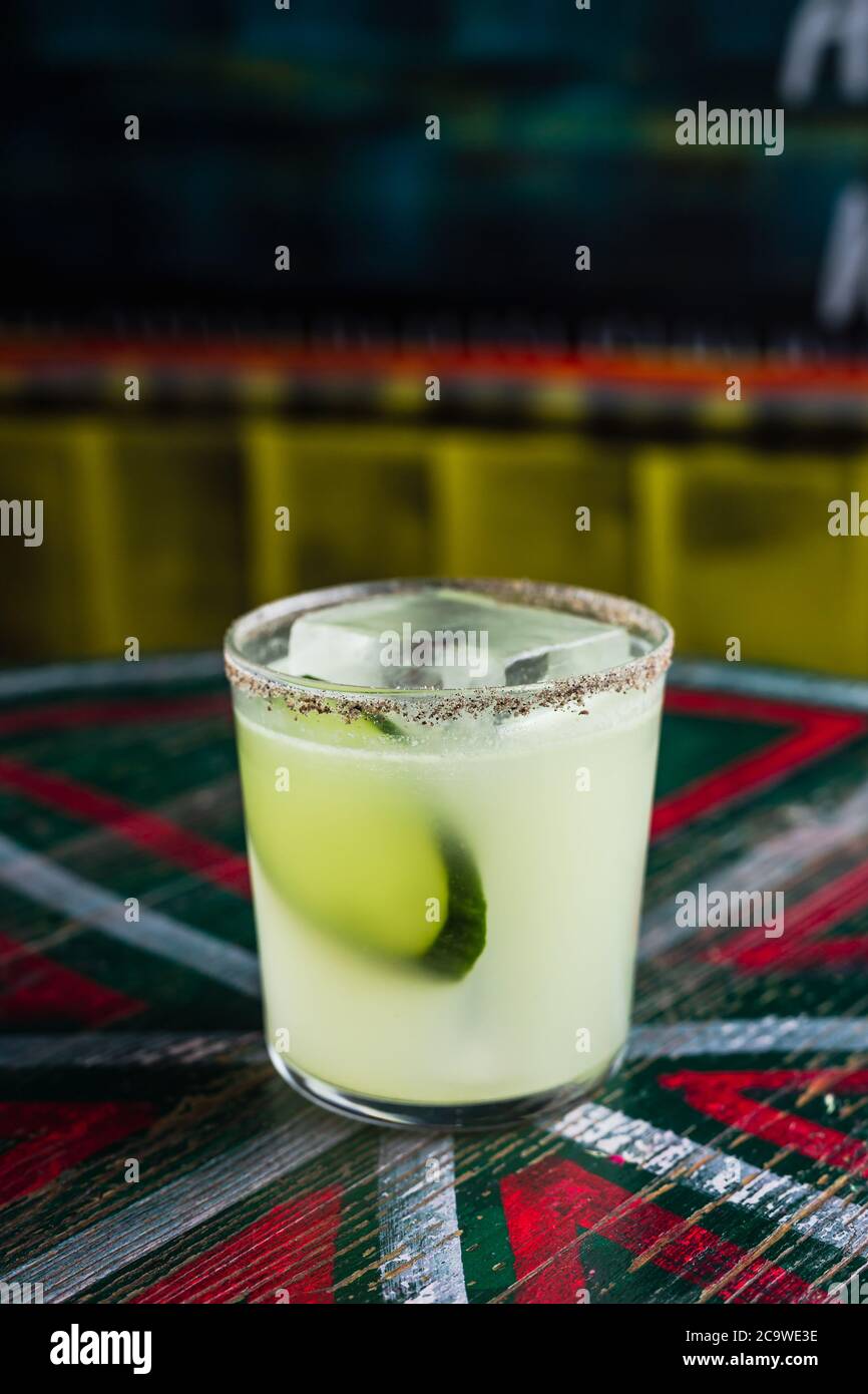 Un cocktail dans un verre de boule de roche avec un grand cube de glace, garni de tranches de concombre, bord épicé sur le verre Banque D'Images