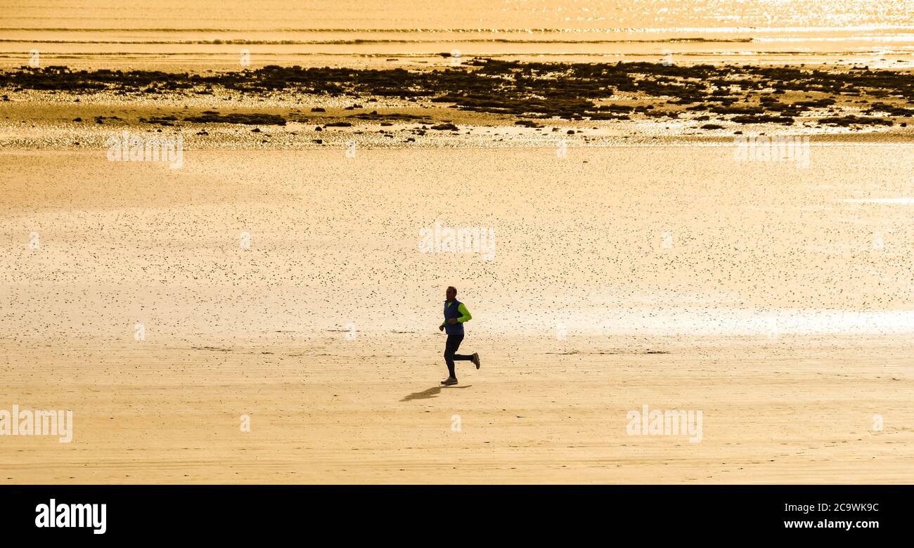 SWANSEA, PAYS DE GALLES - OCTOBRE 2018 : personne seule qui court sur une plage vide à marée basse Banque D'Images