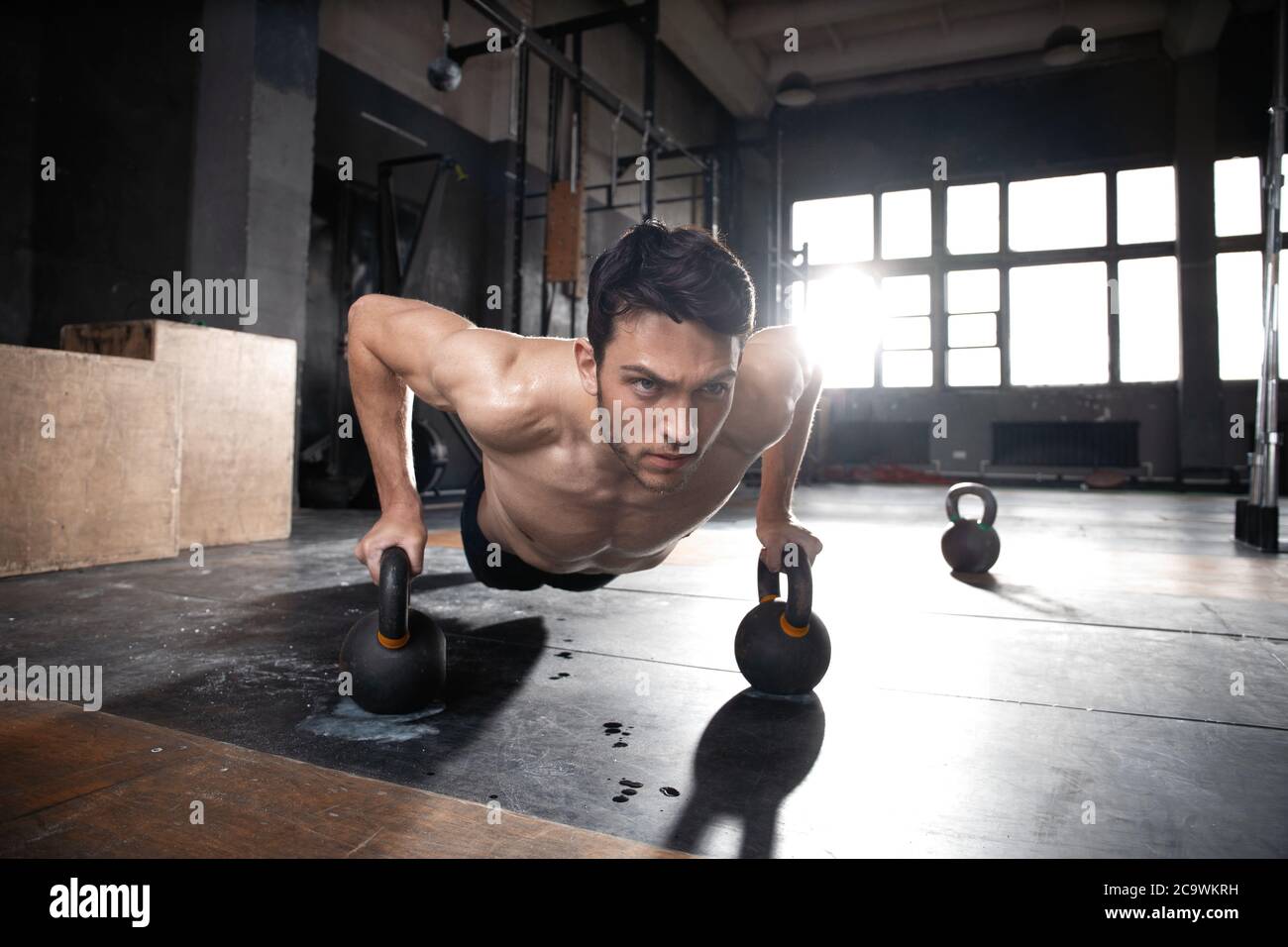 Beau homme musclé faisant un exercice de poussée avec haltères dans un entraînement crossfit. Banque D'Images