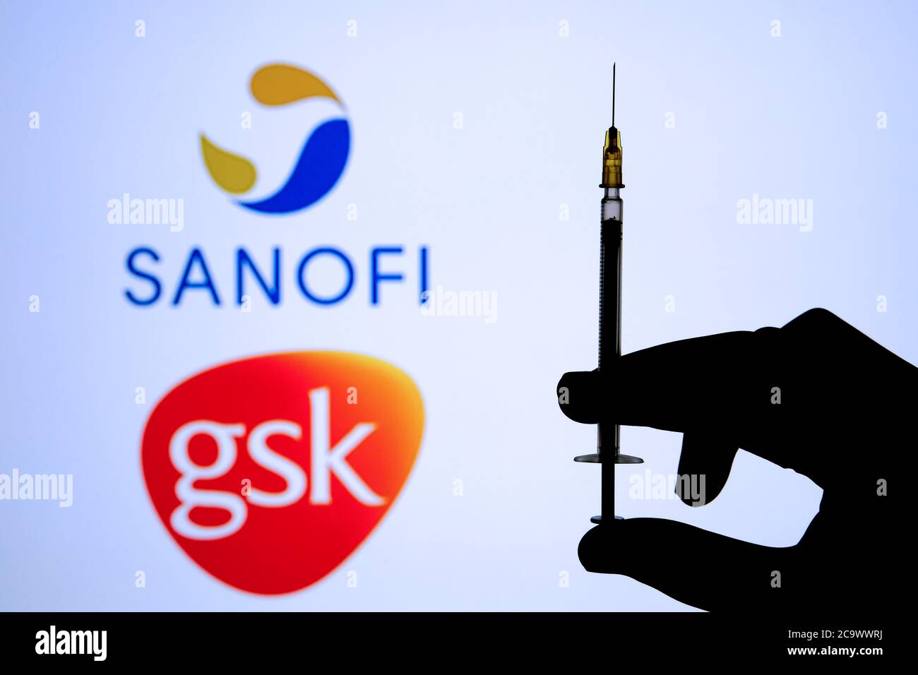 Stone / UK - 2 août 2020 : LOGOS SANOFI GSK sur fond flou et poignée de seringue en silhouette main sur le devant. Concept pour le vaccin COVID-19. Sélection Banque D'Images