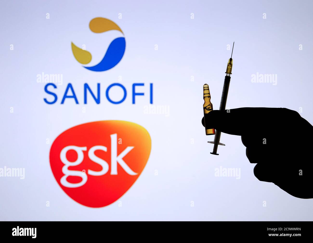 Stone / UK - 2 août 2020 : LOGOS SANOFI GSK sur fond flou et poignée de seringue en silhouette main sur le devant. Concept pour le vaccin COVID-19. Sélection Banque D'Images