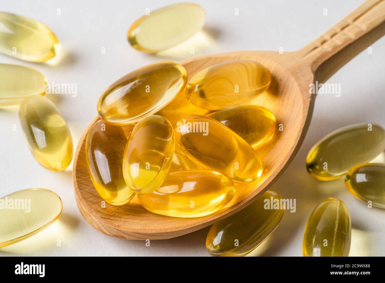 Capsules jaunes Omega 3 dans une cuillère en bois sur fond blanc. EPA et DHA sont deux types d'acides gras essentiels gras oméga-3. Banque D'Images