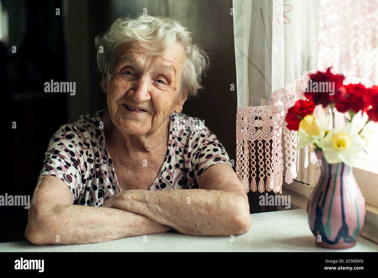 Portrait d'une vieille femme pensionnée assise à la cuisine dans sa maison. Banque D'Images