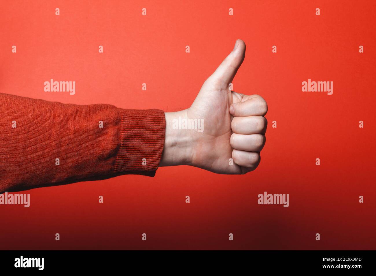La main de l'homme montre le pouce vers le haut sur fond rouge. Banque D'Images
