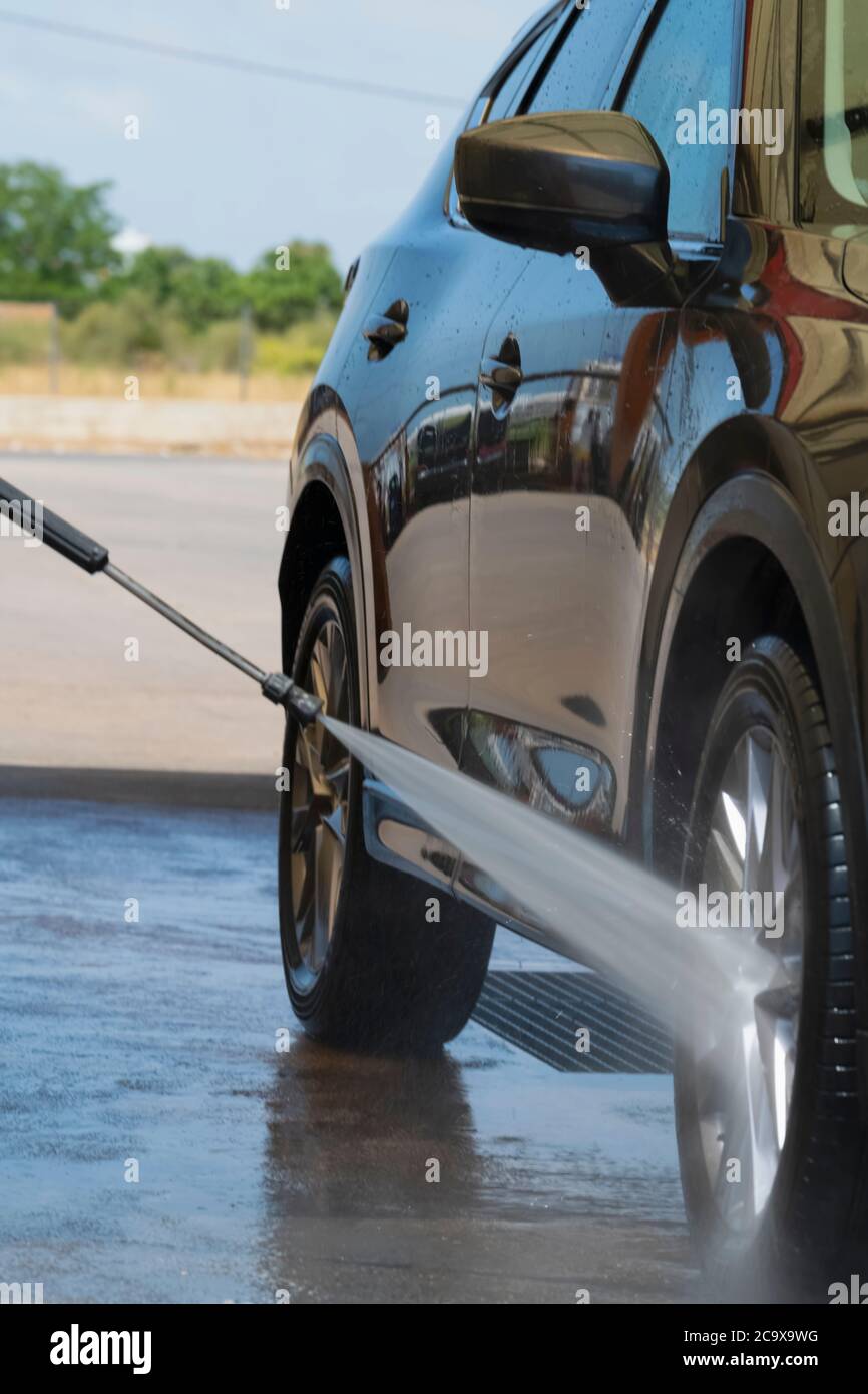 La roue avant d'une voiture est rincée à l'aide d'un jet d'eau haute pression sur un arrière-plan défocacé. Concept de lavage et de nettoyage de voiture. Banque D'Images