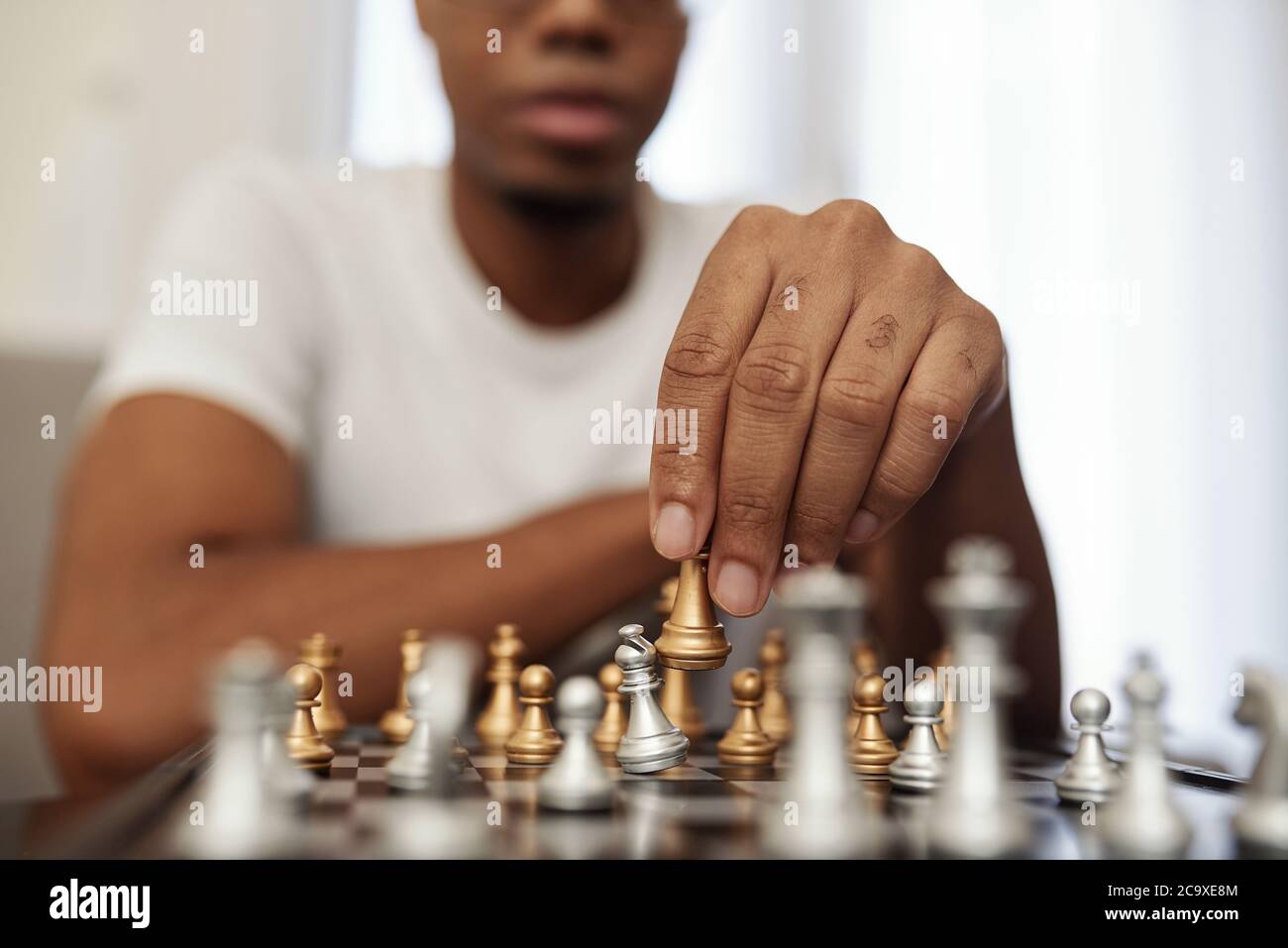 Concentré jeune Noir homme appréciant jouer aux échecs lors de rester à la maison pendant la quarantaine Banque D'Images