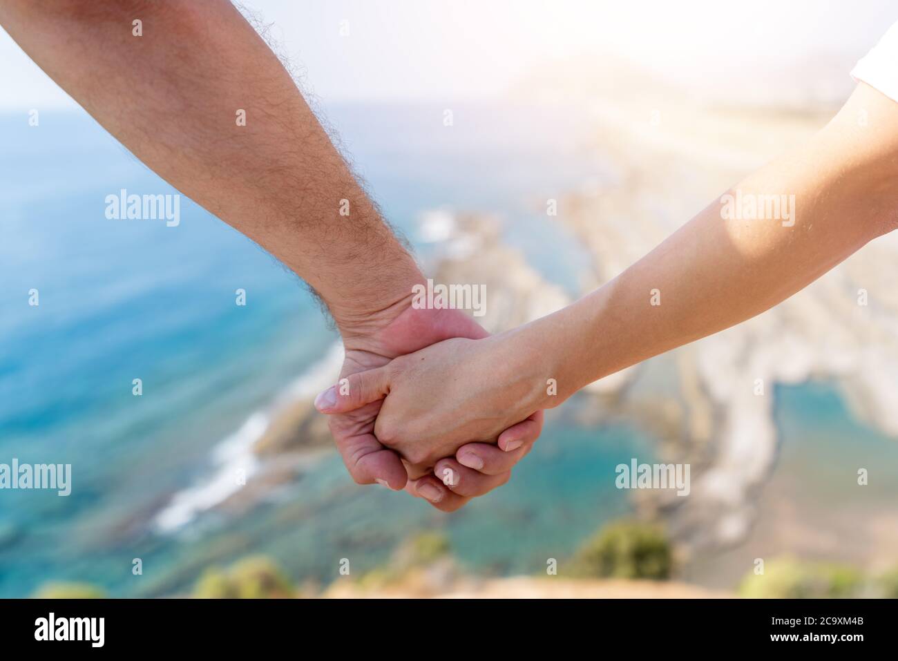 Deux mains se tiennent avec la lumière du soleil floue et la vue magnifique sur le paysage d'une falaise et de la mer. Photo de haute qualité Banque D'Images