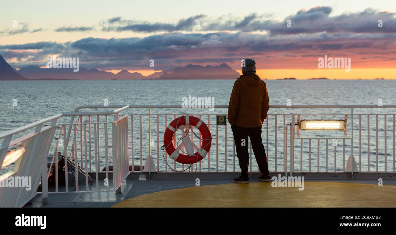 Un homme se tient sur le pont du ferry et observe le coucher de soleil sur l'océan Atlantique. Soleil polaire Banque D'Images