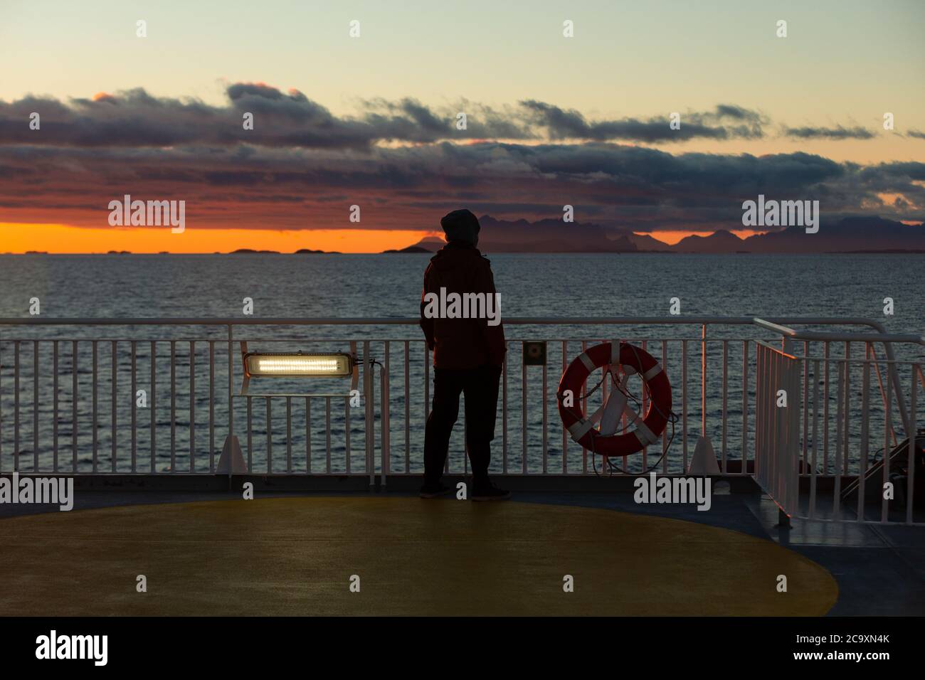 Un homme se tient sur le pont du ferry et observe le coucher de soleil sur l'océan Atlantique. Soleil polaire Banque D'Images