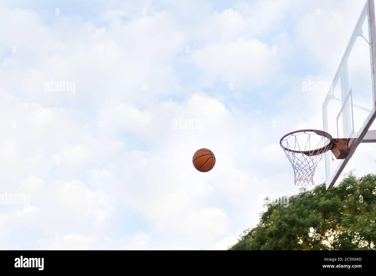 Le ballon s'envole dans le panier de basket-ball. Vue latérale. Ciel avec nuages en arrière-plan. Concept de jeux sportifs. Banque D'Images