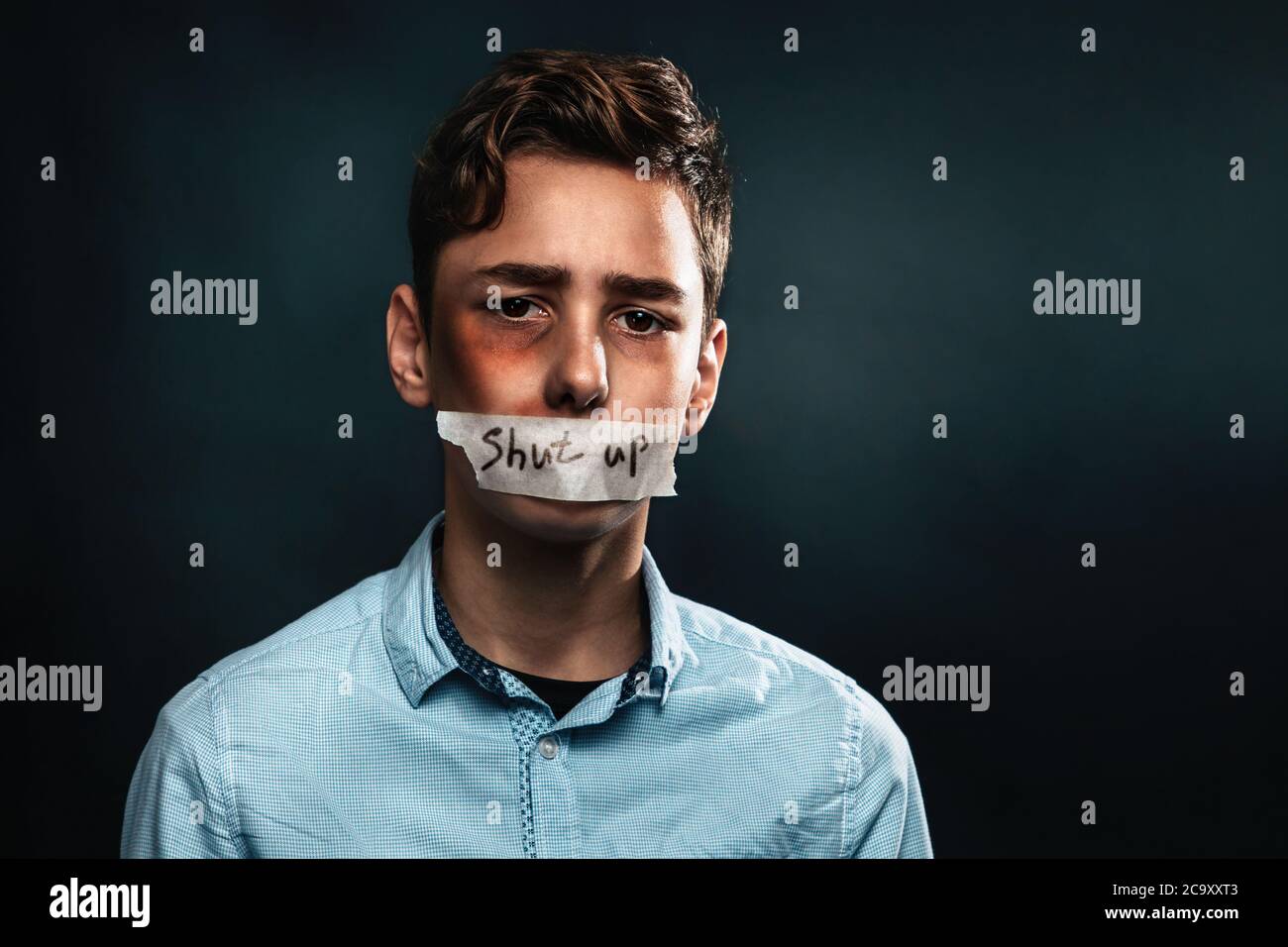 Le concept de violence domestique. Portrait d'un adolescent avec sa bouche fermée par ruban adhésif, ce qui dit Tais-toi. Arrière-plan noir. Copier l'espace Banque D'Images
