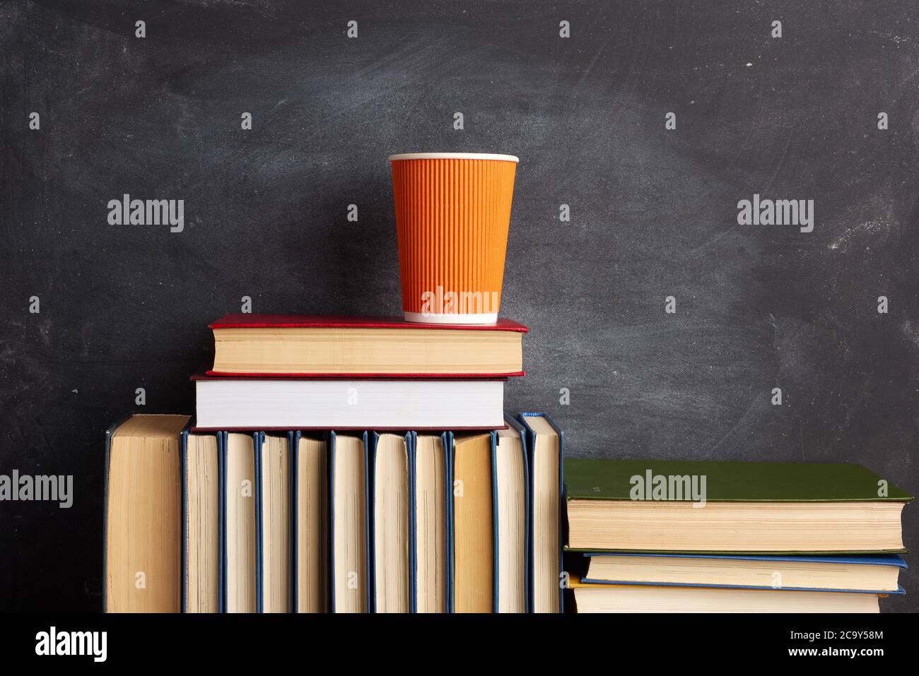 pile de différents livres et une tasse jetable orange avec du café sur fond noir tableau de craie, gros plan Banque D'Images