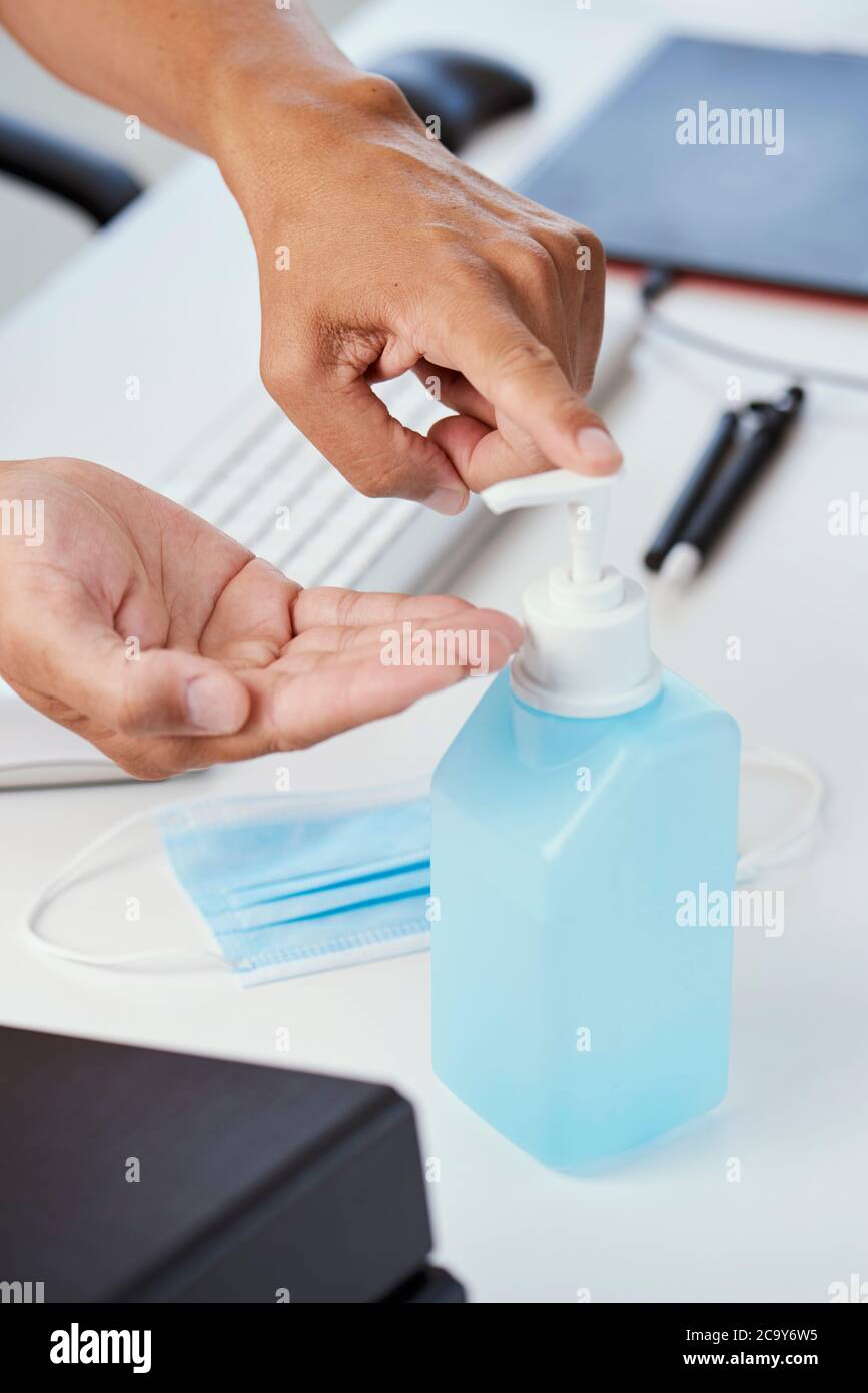 gros plan d'un jeune homme caucasien assis à son bureau désinfectant ses mains avec un désinfectant pour les mains Banque D'Images