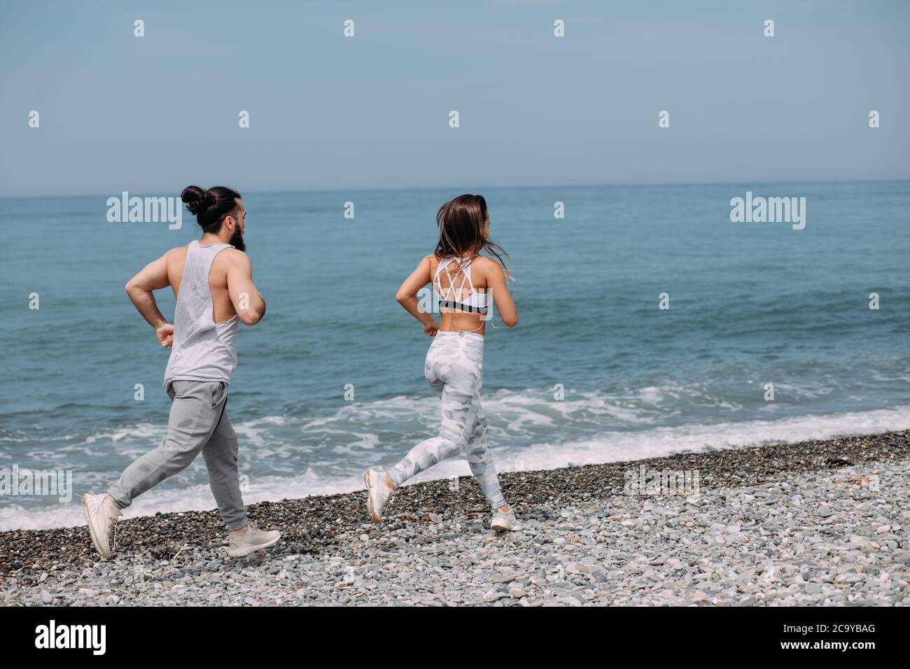 Fitness, sport, personnes et activités santé concept - couple heureux avec vos écouteurs fonctionnant sur une plage de galets au fond de la mer avec copyspace Banque D'Images