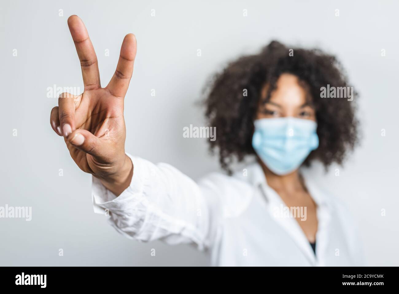 main droite d'une jeune femme afro utilisant un masque chirurgical et faisant le symbole de victoire avec les doigts Banque D'Images