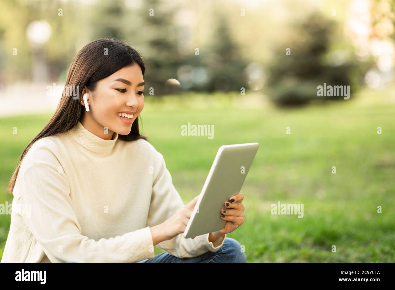 Femme asiatique étudiant utilisant une tablette, assis dans le parc Banque D'Images