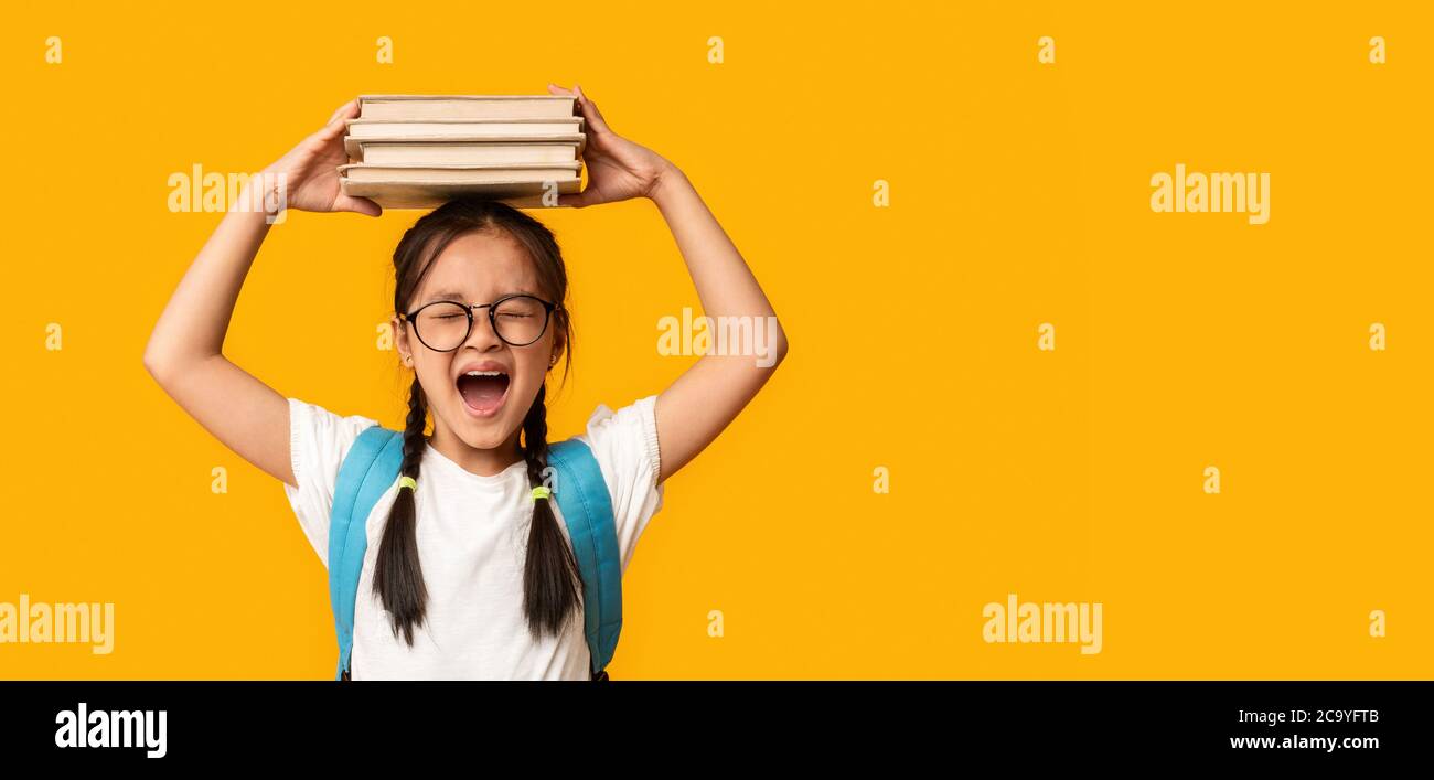 Une écolière asiatique émotive criant en posant avec des livres sur fond jaune Banque D'Images