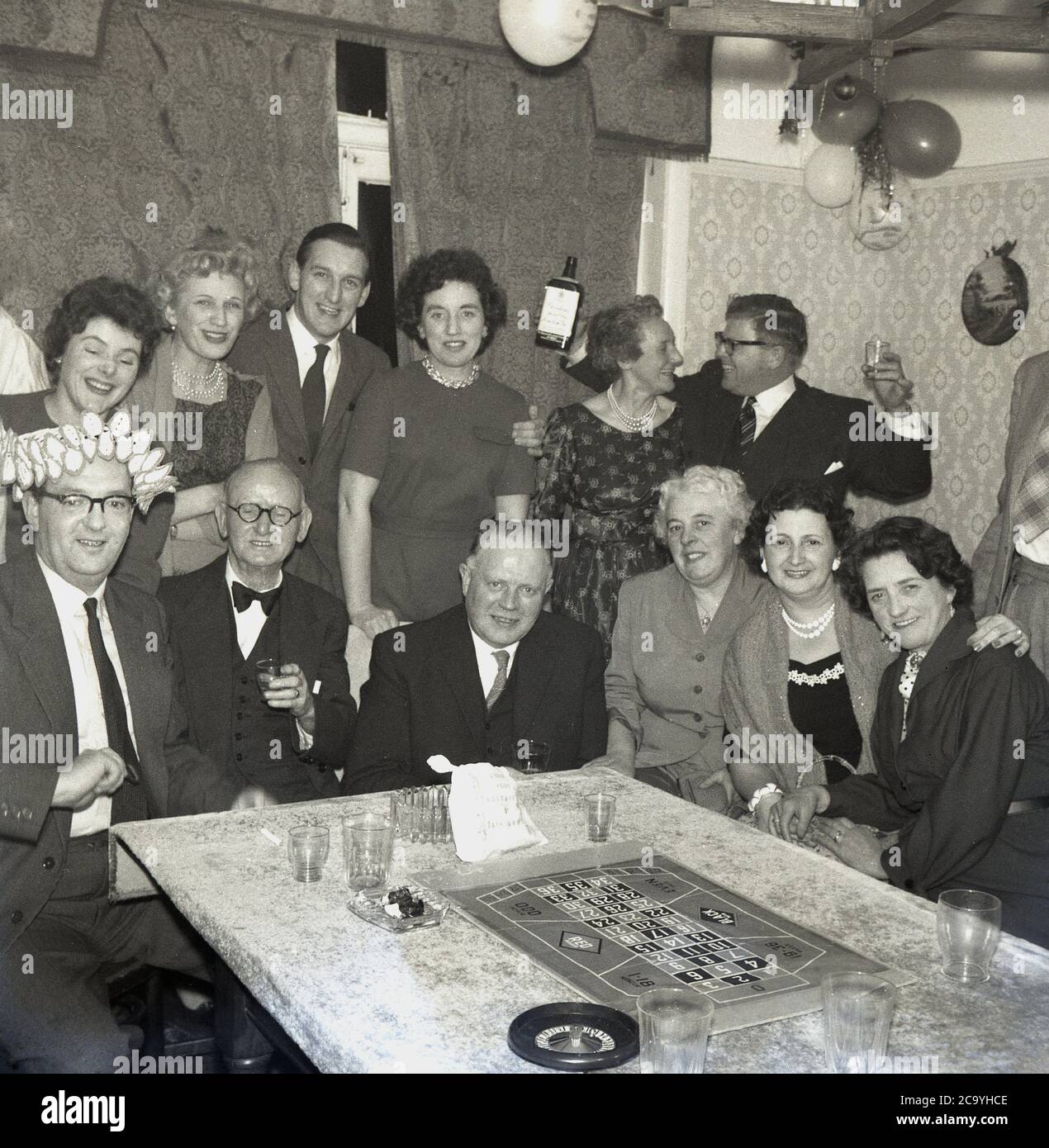 1960 Historique Fete D Anniversaire Adulte Dans Une Maison Hommes Et Femmes Bien Habilles Celebrant Avec Quelques Boissons Gin Et Un Jeu De Roulette De Table Avec Une Petite Roue Et Le Conseil