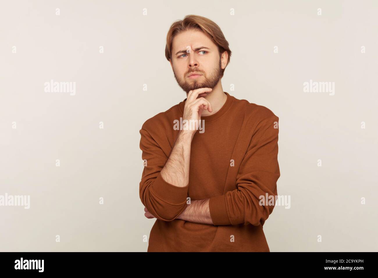 Portrait d'un homme intelligent pensif réfléchi avec des cheveux soignés et une barbe en sweat-shirt touchant le menton tout en pensant intensément, en ayant des doutes, incertain à propos Banque D'Images