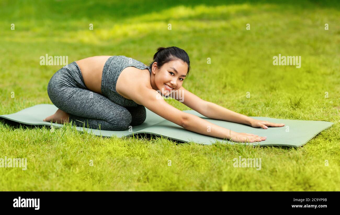 Belle femme asiatique faisant poser l'enfant sur le tapis de yoga au parc vert Banque D'Images