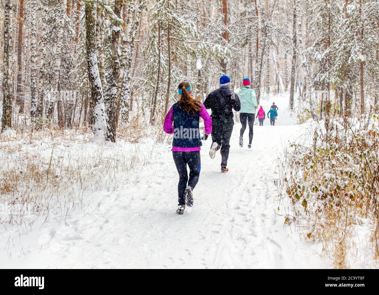 les coureurs du groupe arrière font une course de sentier d'hiver en forêt pendant une chute de neige Banque D'Images