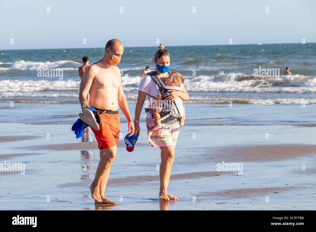 Punta Umbria, Huelva, Espagne - 2 août 2020 : couple avec un bébé marchant sur la plage et portant un masque facial de protection ou médical. Nouvelle norme en Espagne wi Banque D'Images