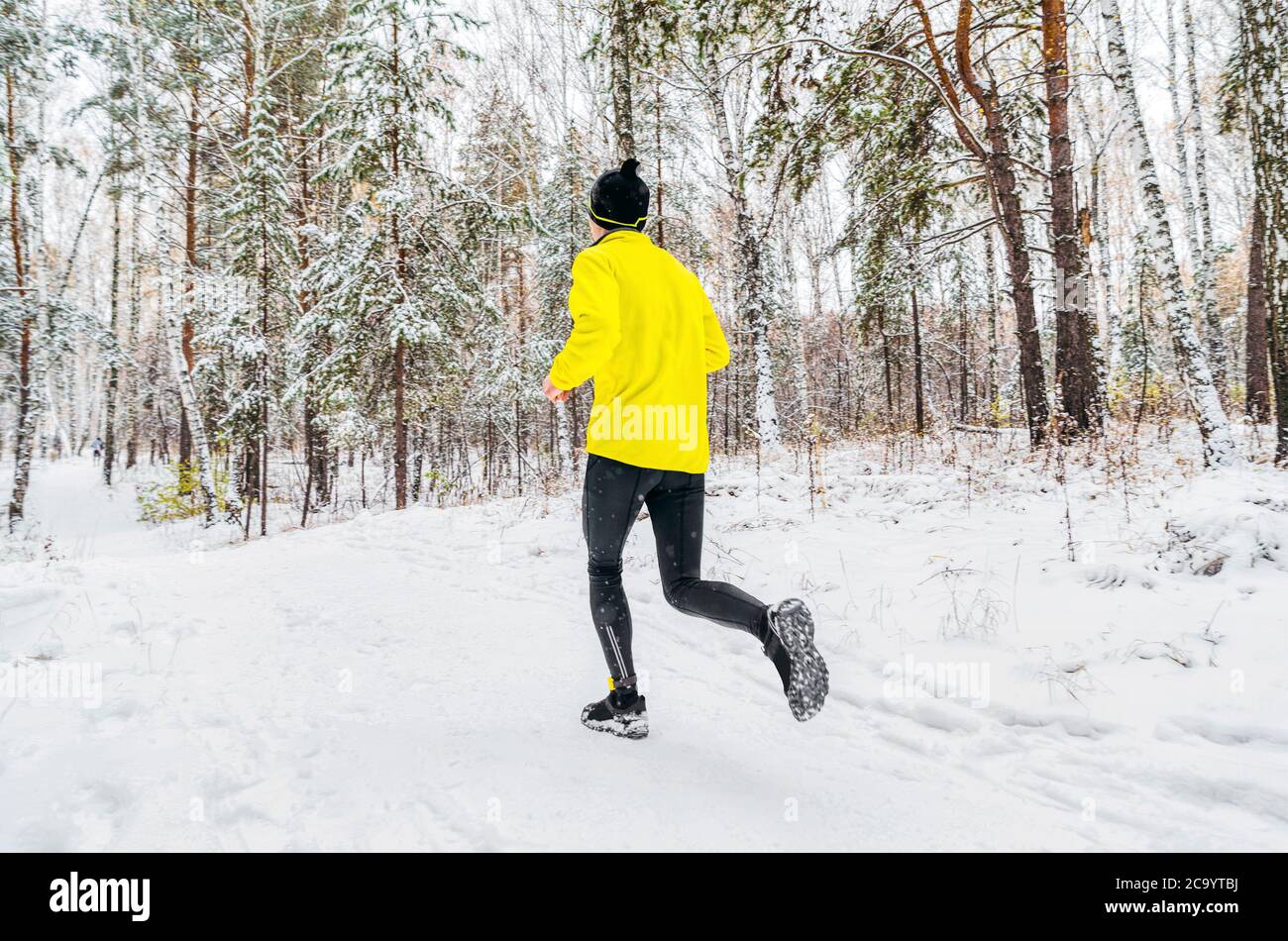 homme athlète coureur en blouson jaune courir hiver forêt trail course Banque D'Images