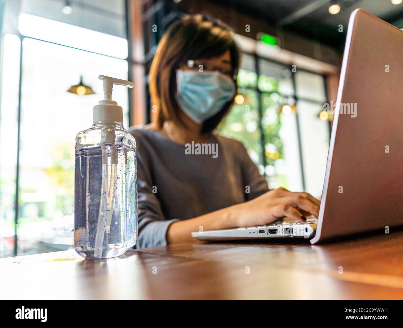Jeune femme asiatique utilisant un ordinateur portable travaillant à la maison avec du gel d'alcool en quarantaine pour le coronavirus portant un masque de protection avec distanciation sociale Banque D'Images