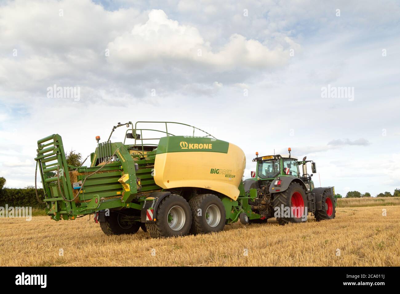 Vue arrière d'un tracteur utilisant une presse à balles de foin dans un champ. Beaucoup Hadham, Hertfordshire. ROYAUME-UNI. Banque D'Images