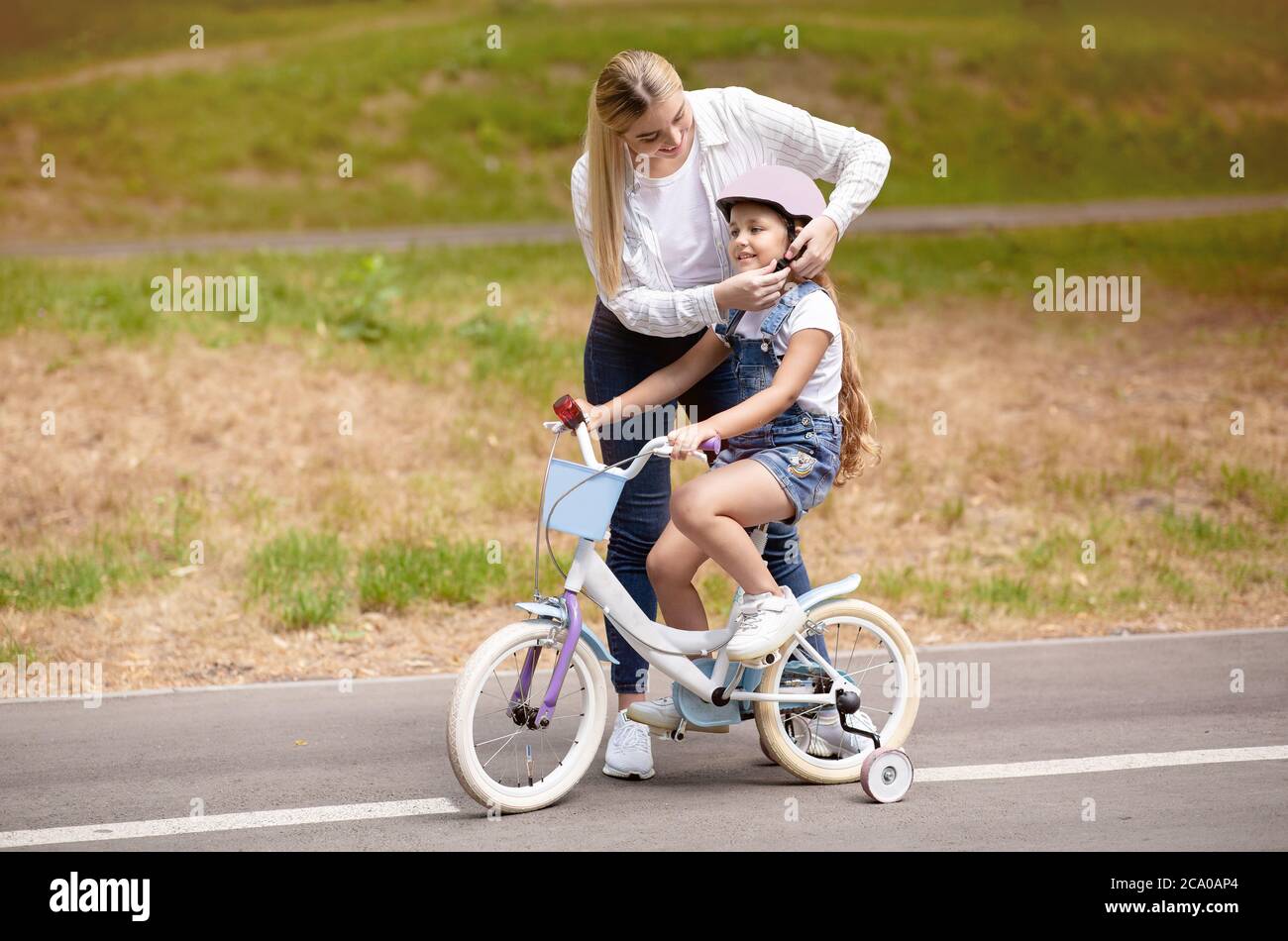 Mère enseignant à la fille de faire du vélo avec des stabilisateurs à l'extérieur Banque D'Images