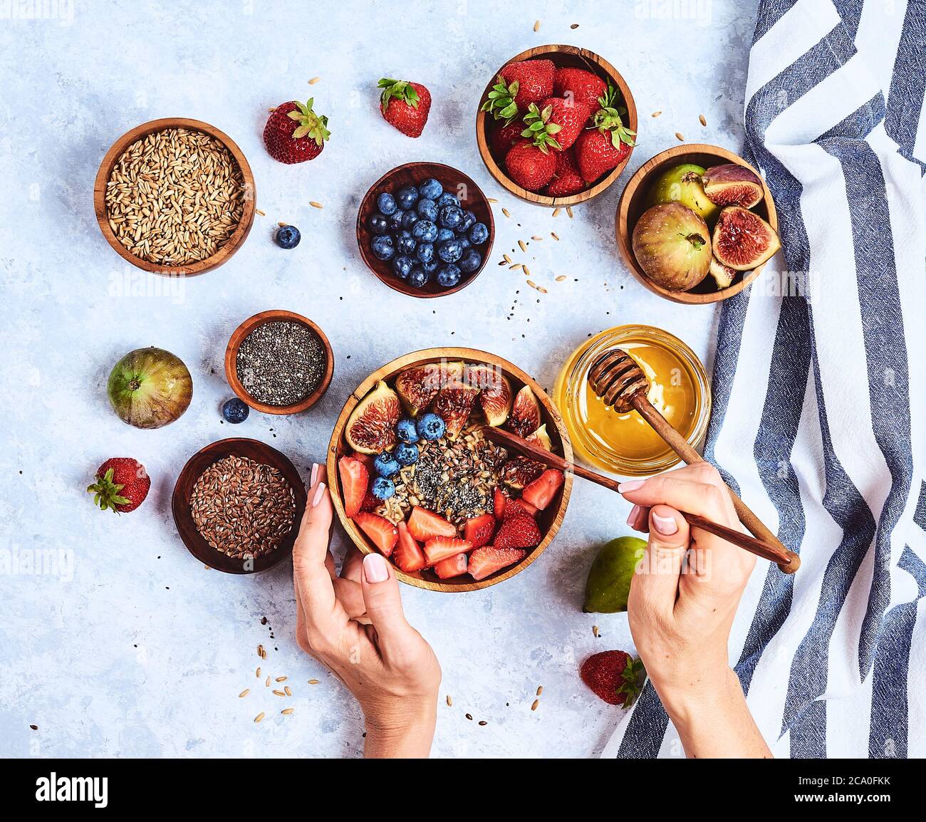 Vue du dessus montrant les mains manger du gruau avec du miel, bleuets, fraises sur fond bleu table en bois bonjour, petit-déjeuner sain Banque D'Images