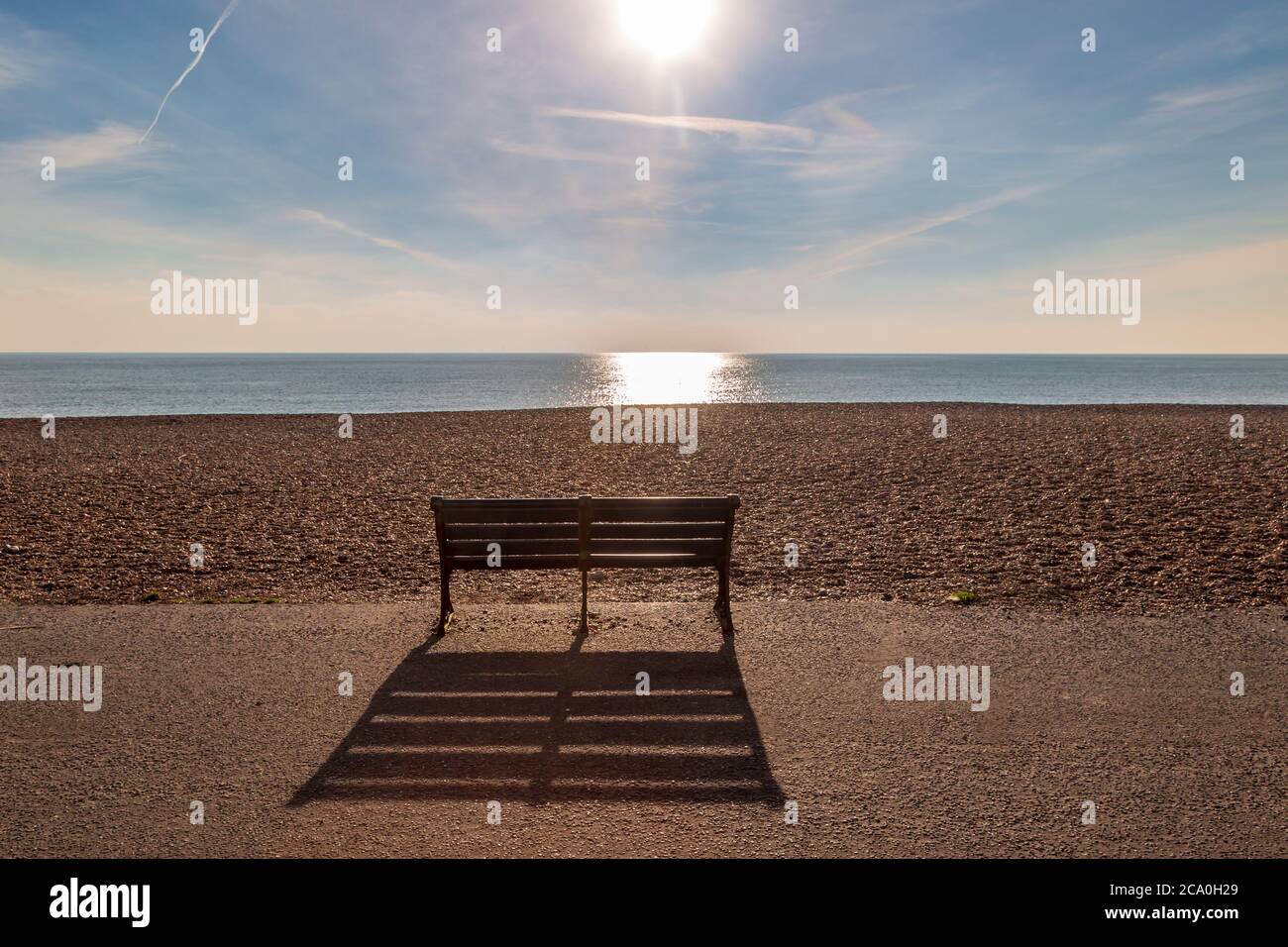 Un banc vide sur le front de mer, jetant une longue ombre en raison du soleil d'hiver bas Banque D'Images