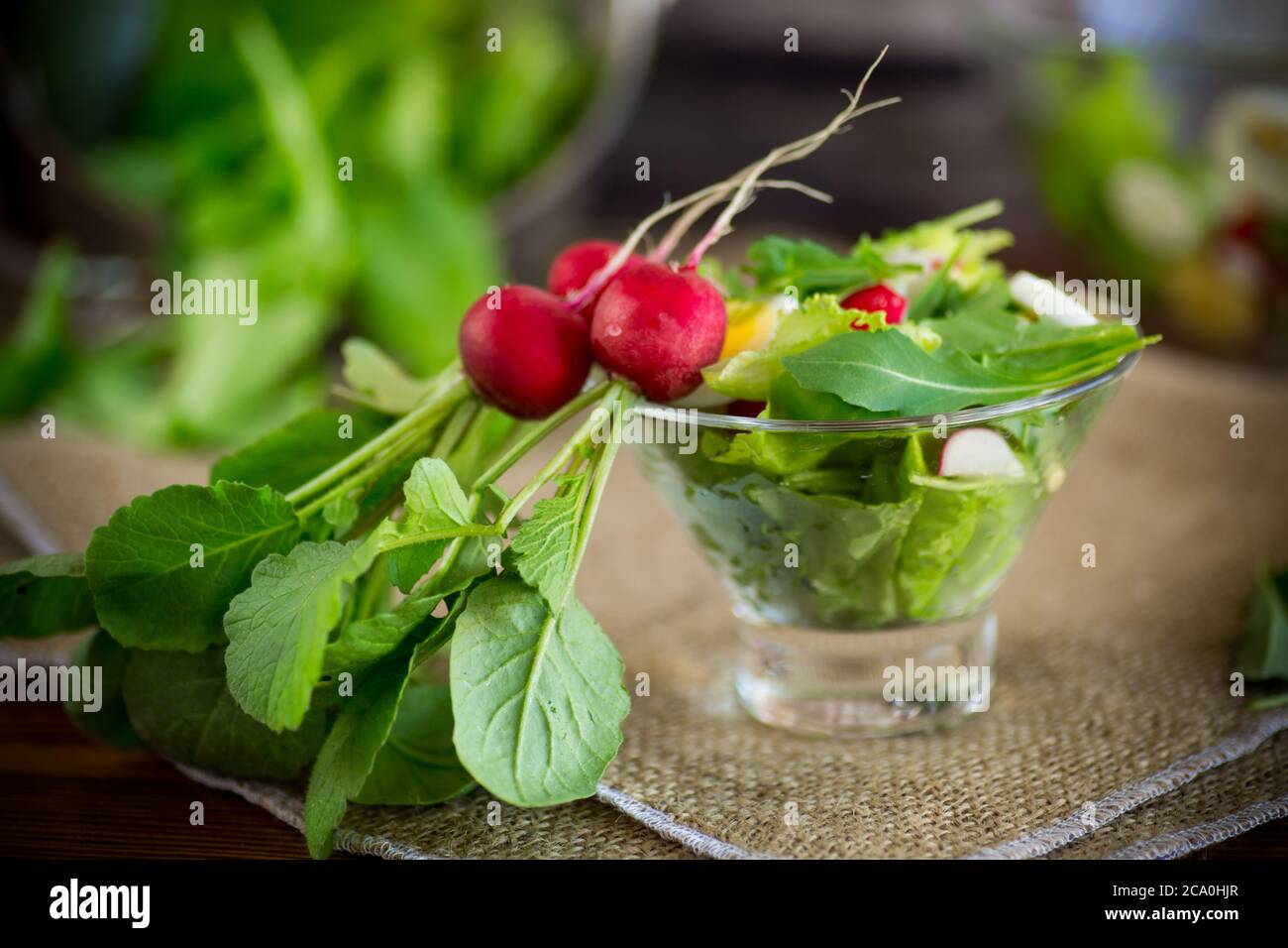 salade de printemps avec une rugula, des œufs durs, du radis frais, des feuilles de salade dans un bol en verre sur une table en bois Banque D'Images