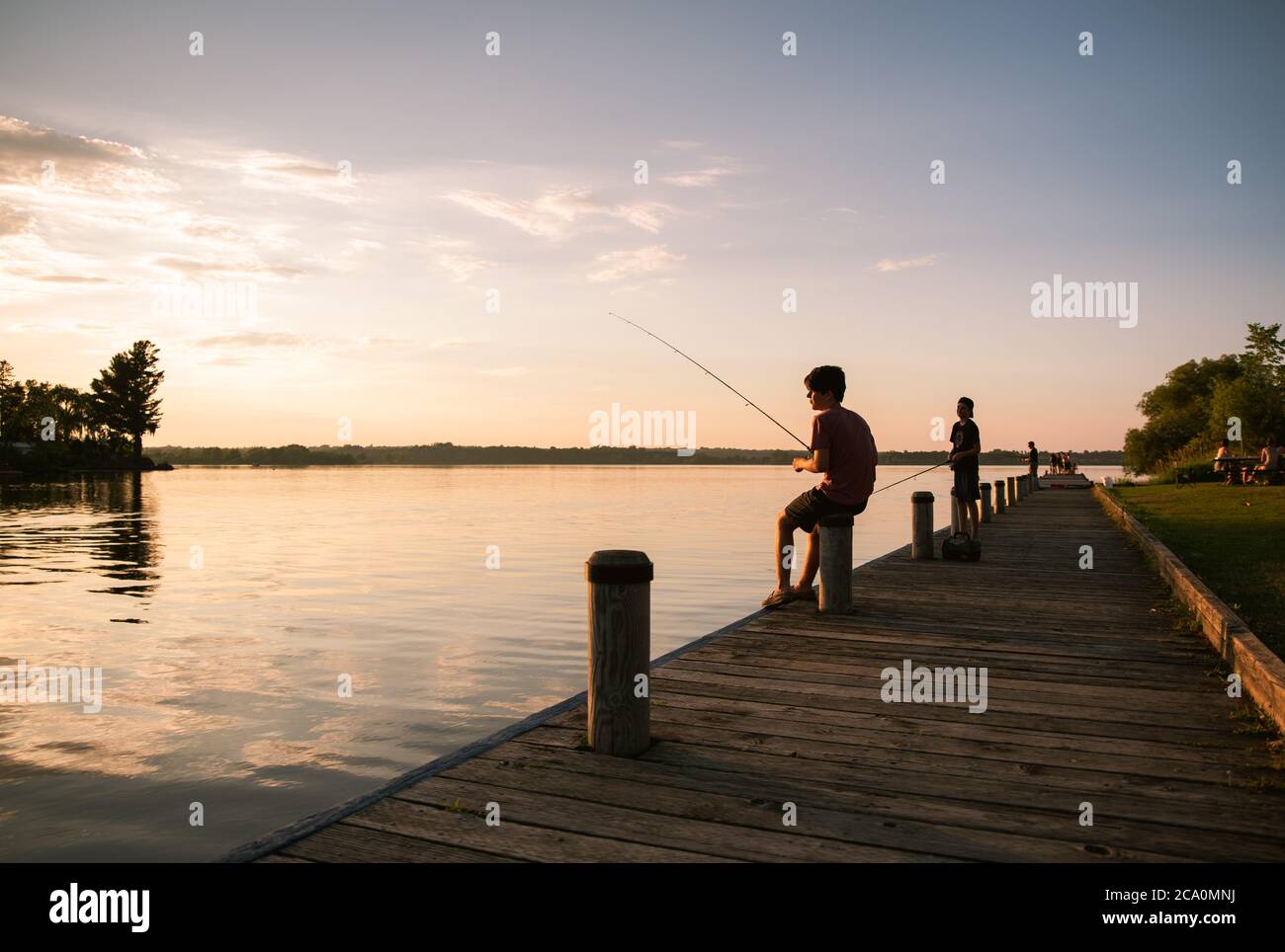 Garçons pêchant sur le quai d'un lac au coucher du soleil en Ontario, Canada. Banque D'Images