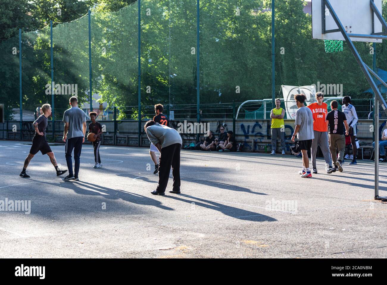 Des jeunes jouant au basket-ball au terrain de basket-ball de Brahenkenttä sous le soleil du soir dans le quartier d'Alppiharju à Helsinki, en Finlande Banque D'Images