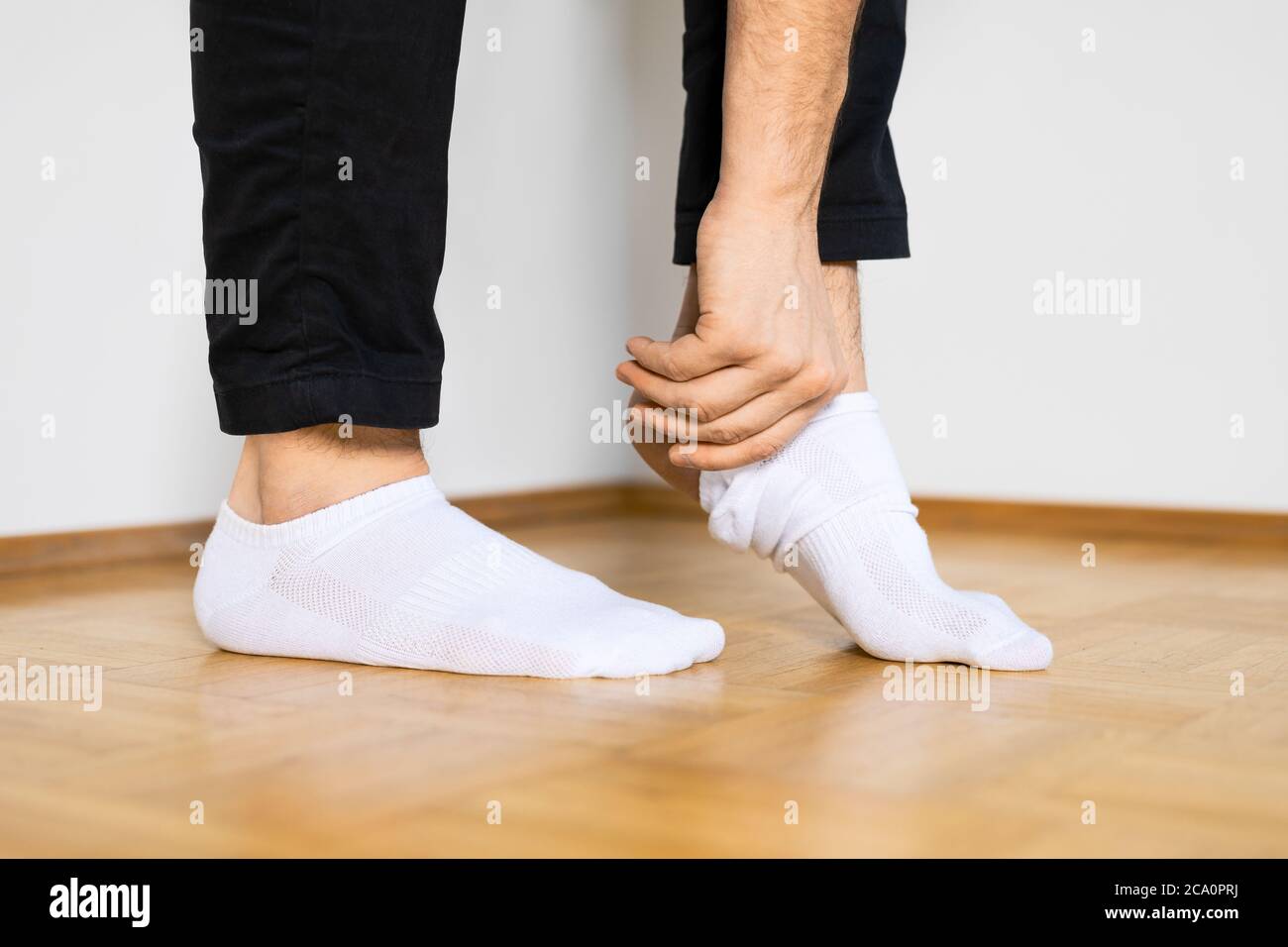 pieds humains mettant sur des chaussettes blanches de cheville en se tenant à la main sur le plancher en bois Banque D'Images
